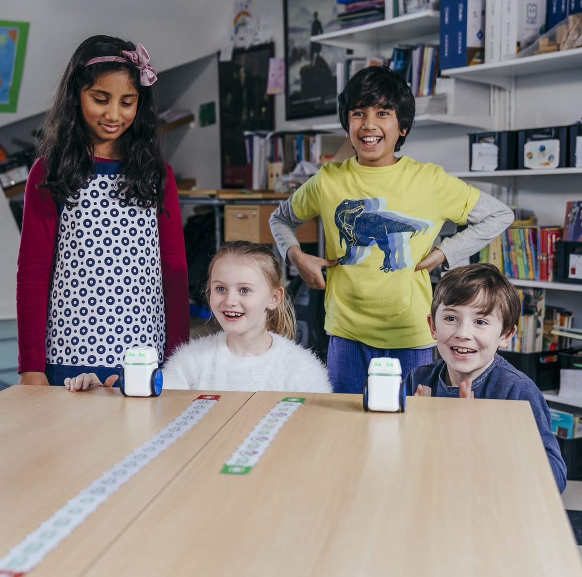 Four students around a classroom table, laughing and cheering as two KUBO robots drive along their TagTile routes