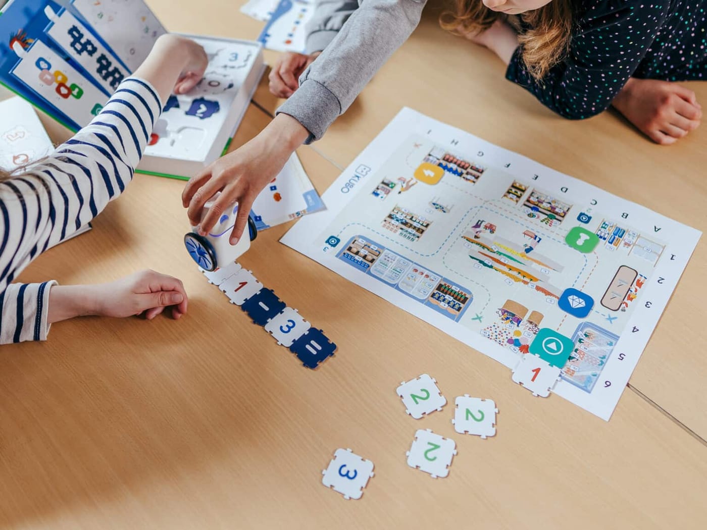 Students' hands snapping TagTiles into a route next to an activity map, one holding the KUBO robot