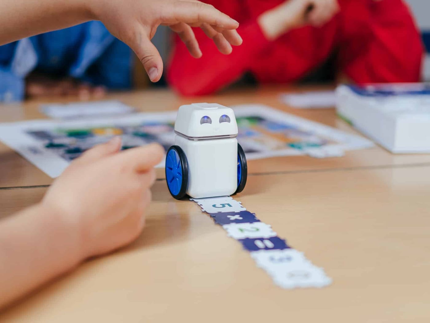 The KUBO robot driving along a row of TagTiles on a desk as a student reaches towards it