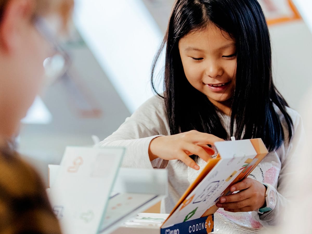A smiling student lifts the lid of a KUBO box at a classroom desk