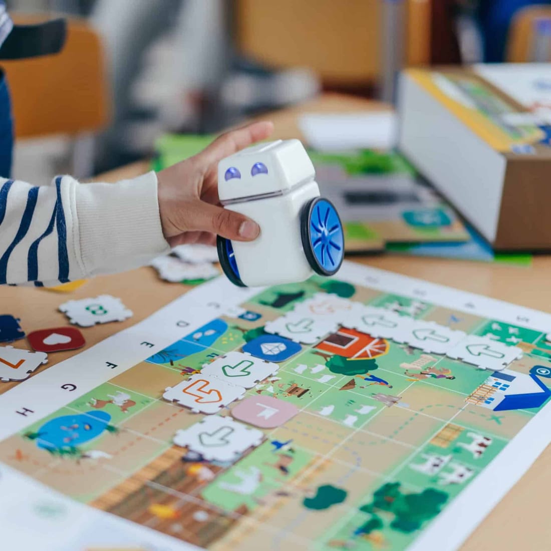 A student's hand places the KUBO robot onto a route of TagTiles laid across an activity map